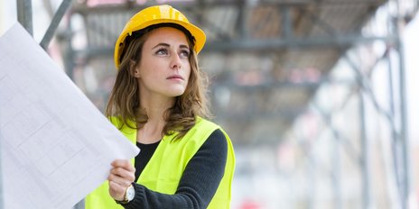 Eine Frau mit Bauhelm hält eine Zeichnung auf einer Baustelle
